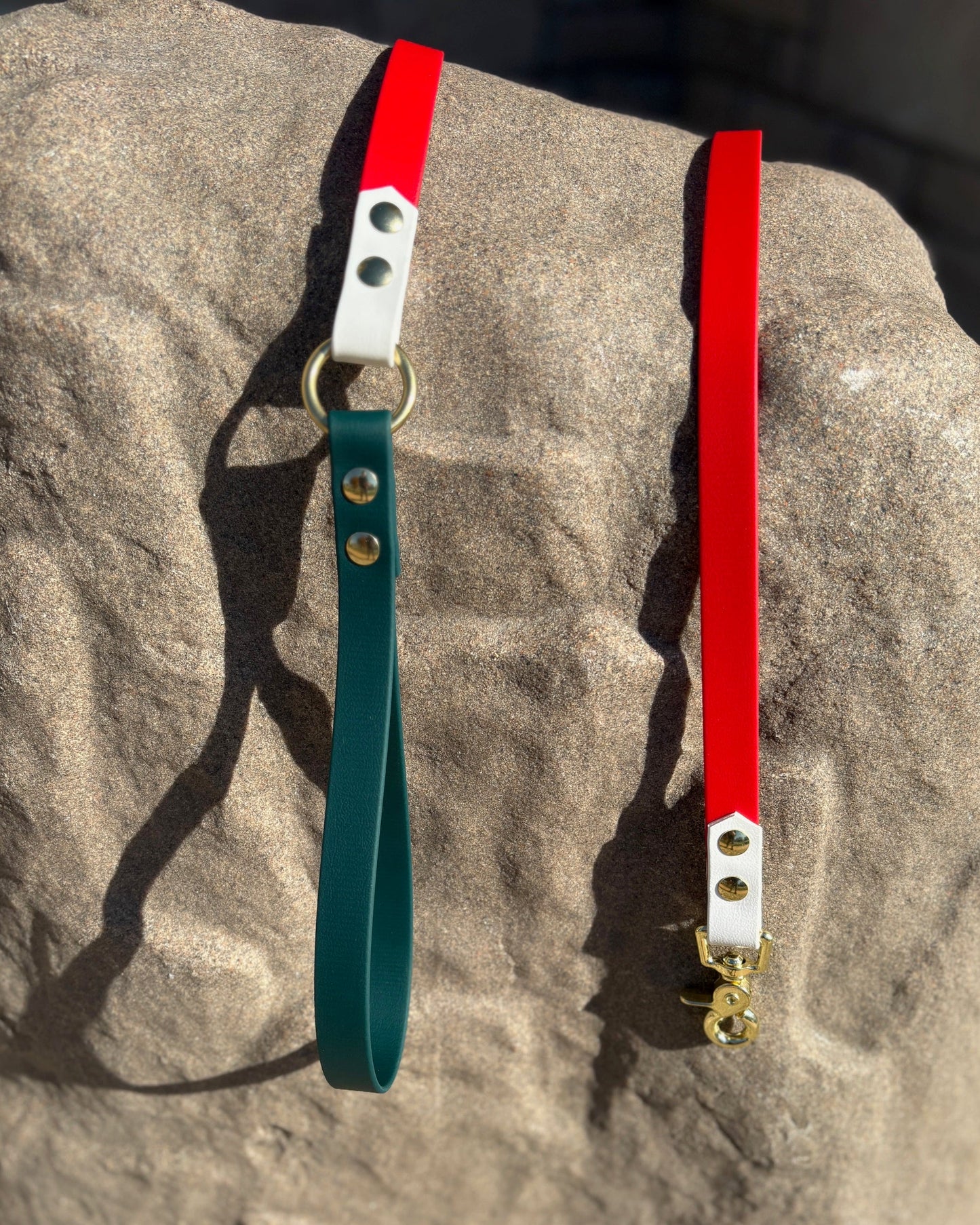 A Classic Evergreen, Arctic White and Cherry Red Classic Leash with gold hardware draped over a large rock