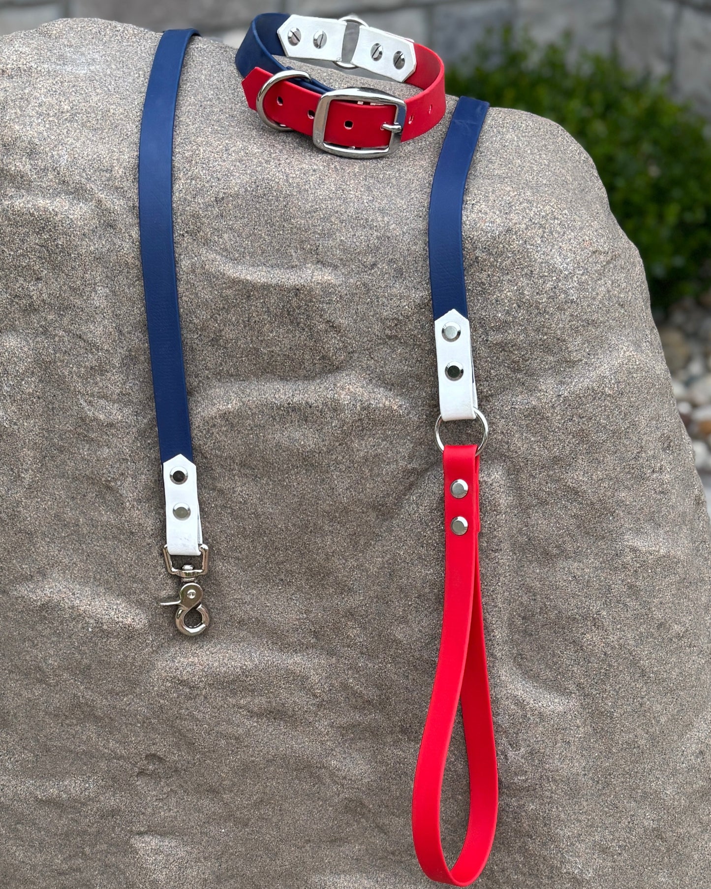 A red, white and blue dog collar with silver hardware sitting on a stone.