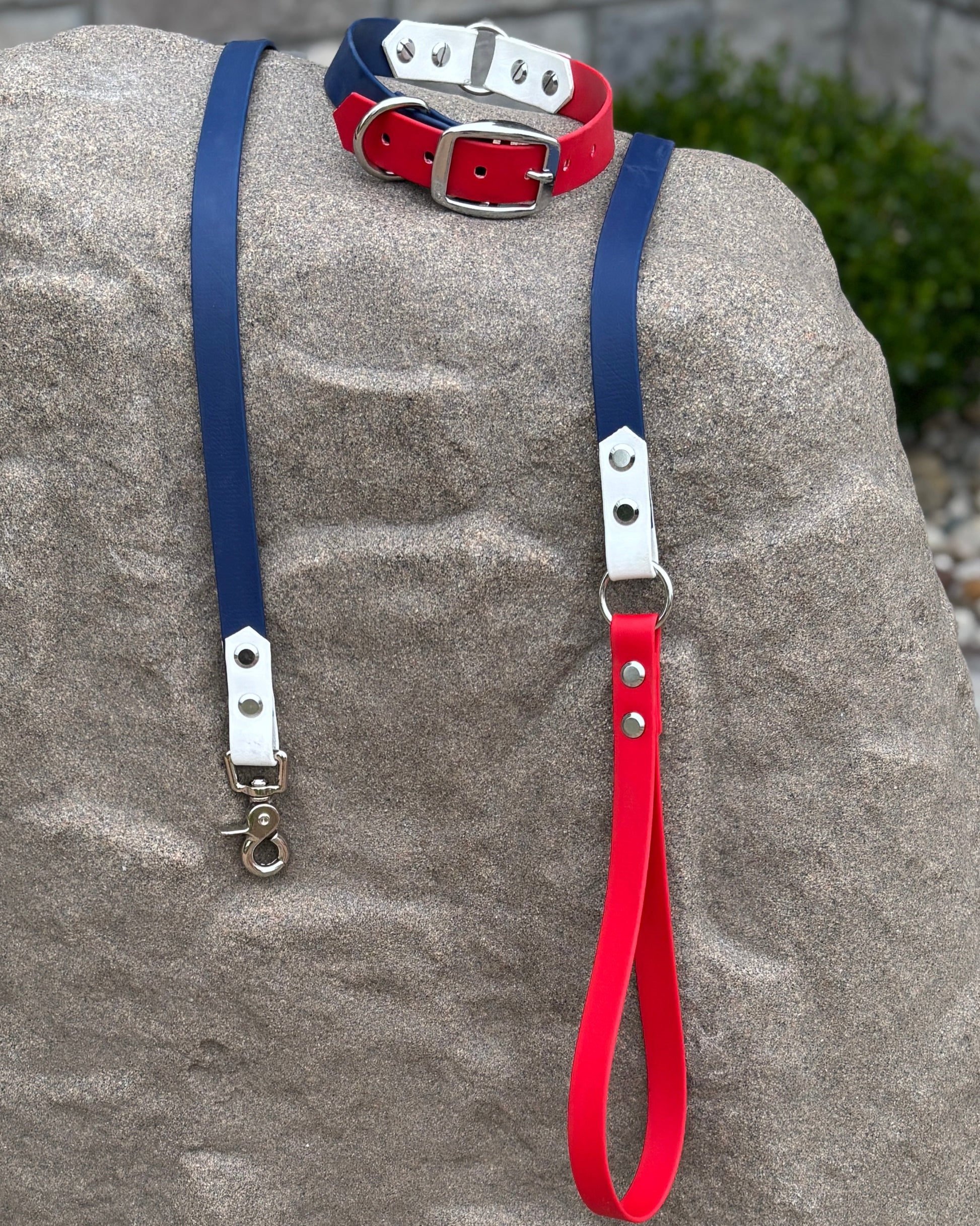 A red, white and blue dog collar with silver hardware sitting on a stone.