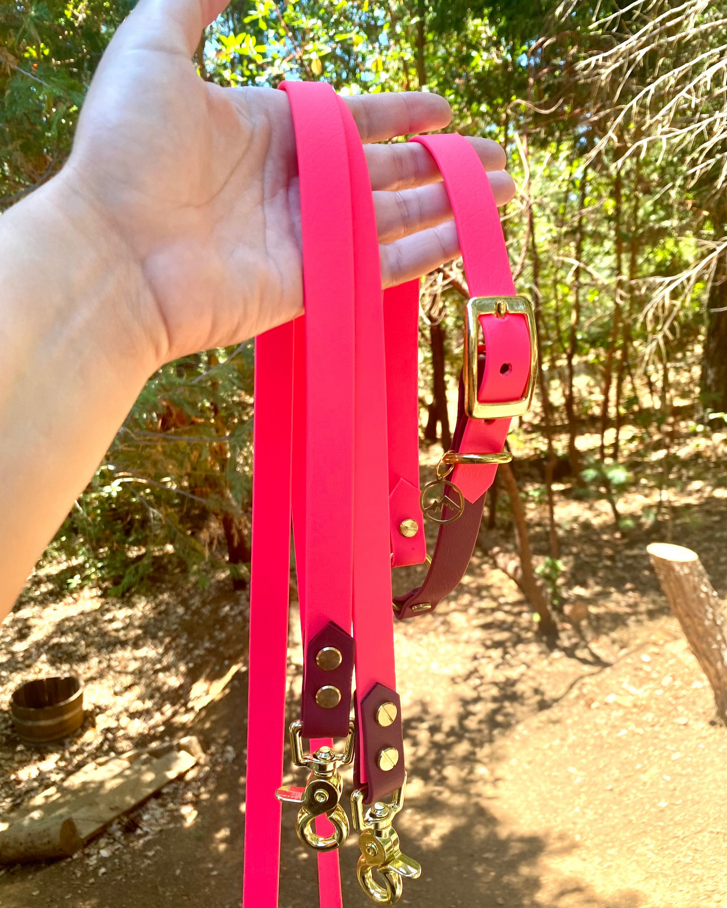 A person holding a two tone Multiway leash in the woods. The leash is hot pink and brown with gold hardware.