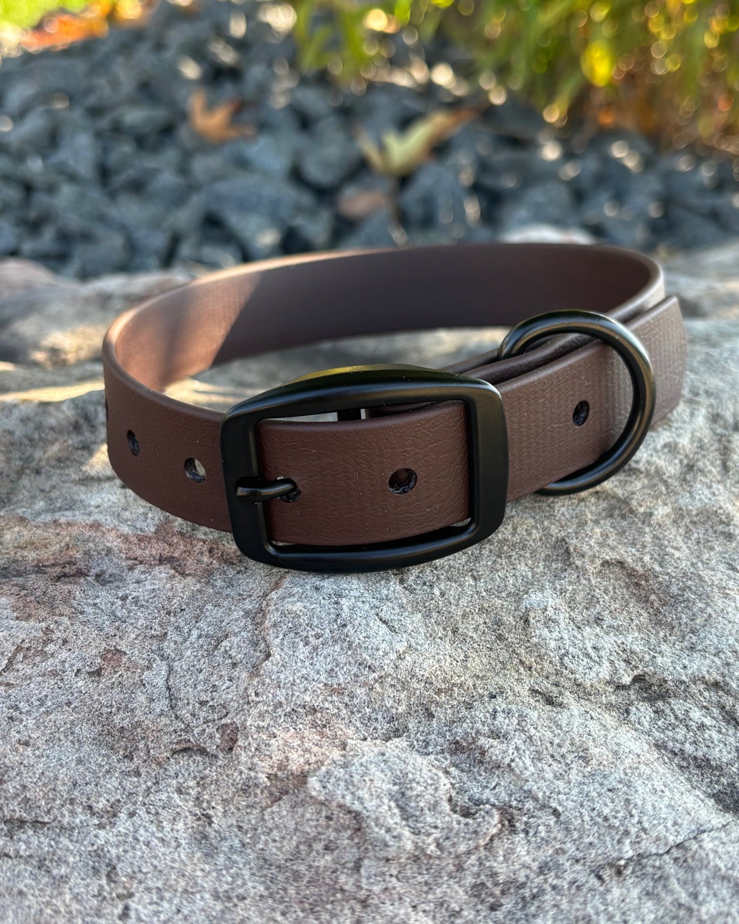 A Rustic Brown Classic Dog Collar resting on a rock. The collar has black hardware