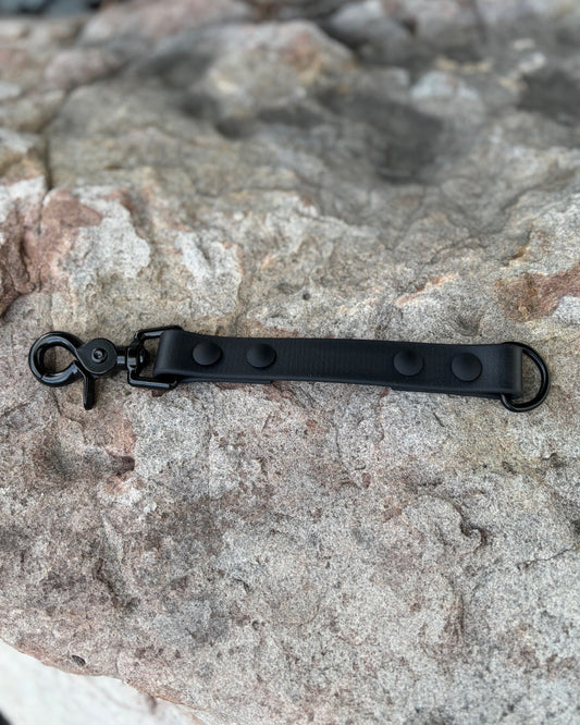 A StraightLine GearSnap made from Evergreen Dog Co placed on a rock. The material is Midnight Black color with a black trigger snap and black O-Ring