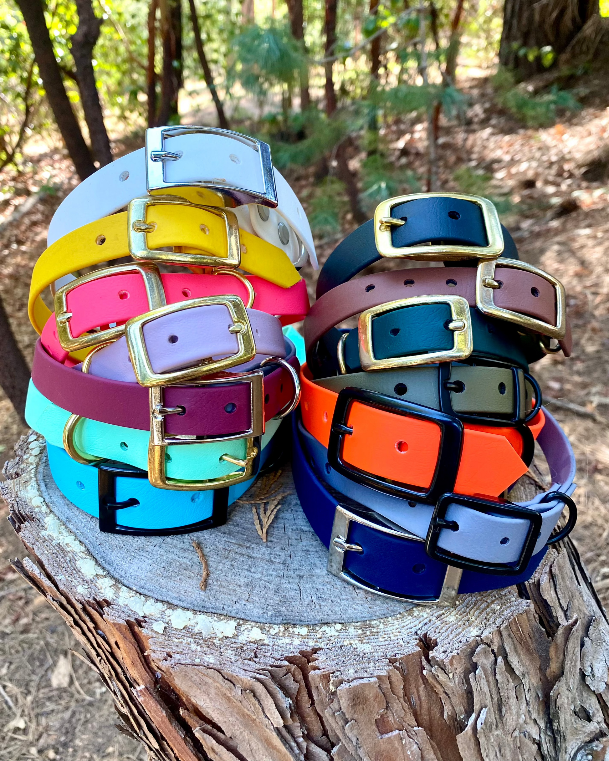 A stack of BioThane dog collars on a log. They are multiple colors. 