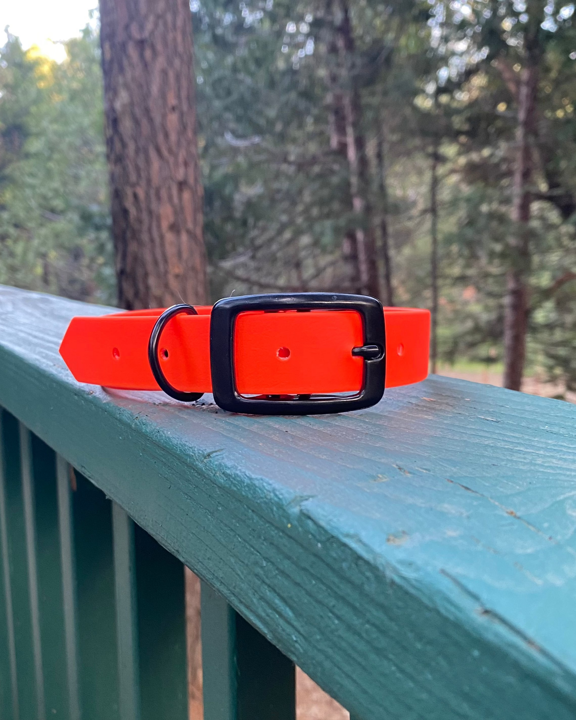 A blaze orange waterproof dog collar sitting on a green railing in he woods.