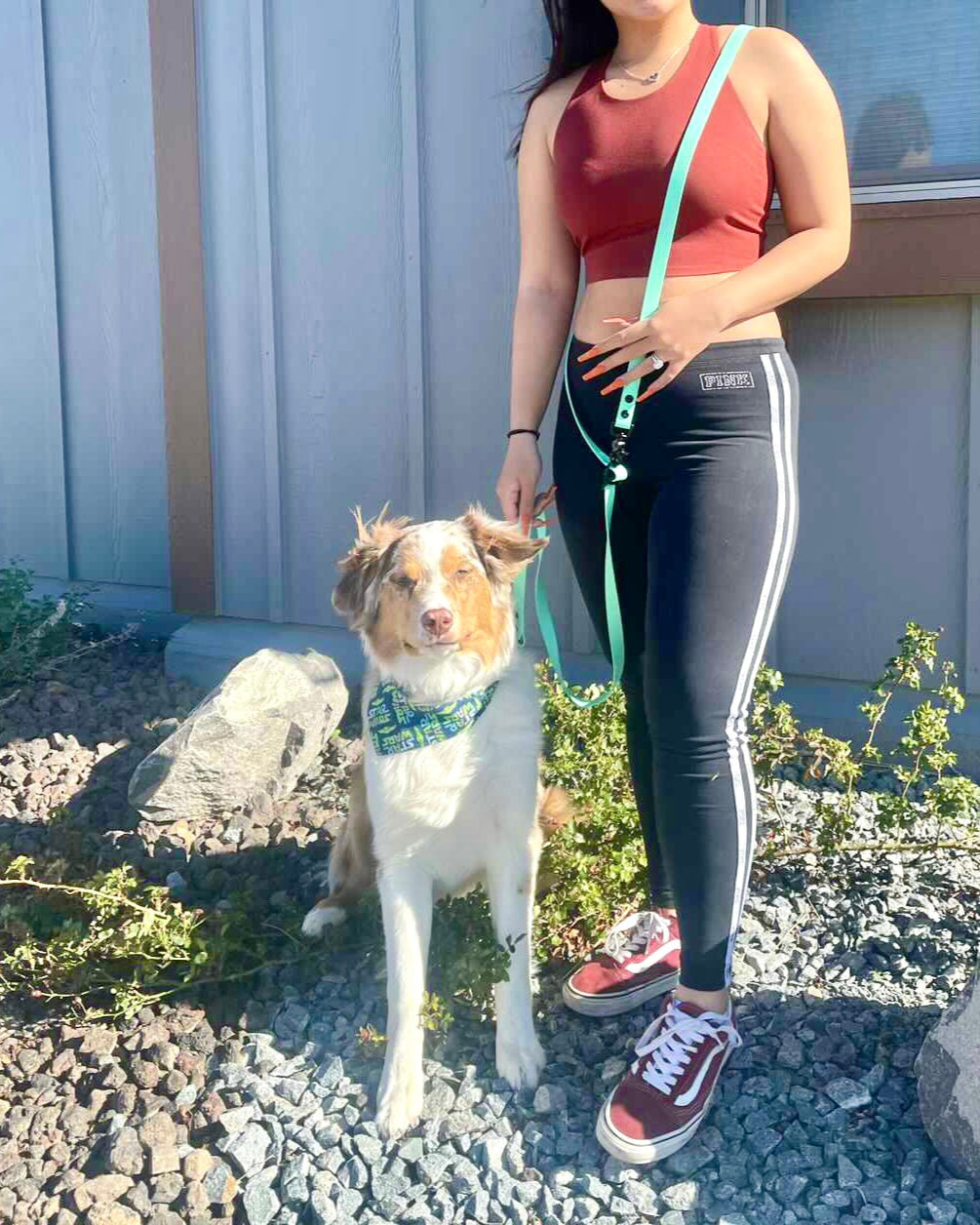 A girl with her dog in front of a building. She is wearing a red top and black paints and also wearing a multiway leash over her shoulder attached to her dog.