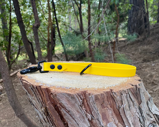 A yellow traffic handle sitting on top of a stump with trees in the background.